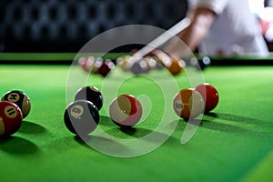 Man\'s hand and Cue arm playing snooker game or preparing aiming to shoot pool balls on a green billiard table. Colorful snooker