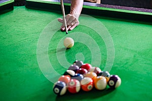 Man\'s hand and Cue arm playing snooker game or preparing aiming to shoot pool balls on a green billiard table. Colorful snooker