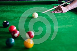 Man`s hand and Cue arm playing snooker game or preparing aiming to shoot pool balls on a green billiard table. Colorful snooker