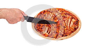 Man`s hand cuts the BBQ pizza with the kitchen knife, angle view. Italian pizza with ham, bbq sauce, bacon and salami, isolated