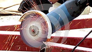 A man's hand cuts off a piece of iron pipe using an angle grinder. Cutting steel interspersed with sparks on a