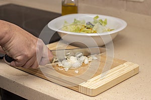 A man`s hand cutting an onion with a knife on top of a wooden board
