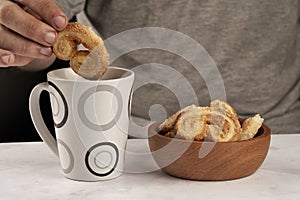 Man's hand dipping puff pastry palmeritas orejitas cup tea coffee photo