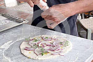 Man`s hand dressing an uncooked onions pizza on a marble table with copy space for your text