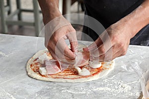 Man`s hand dressing an uncooked   pizza on a marble table with copy space for your text