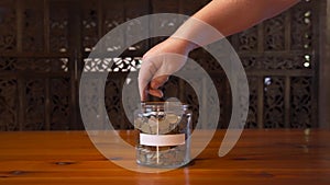 Man`s hand dropping coins in a savings jar with blank label