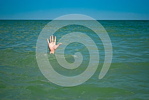 A man`s hand drowns in water calling for help, against the background of the sea and sky clouds summer