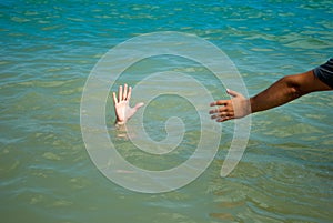 A man`s hand drowns in water calling for help, man helps rescue, against the background of the sea