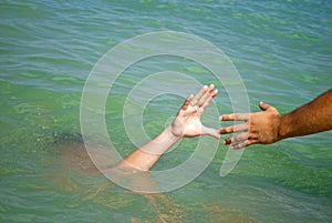 A man`s hand drowns in water calling for help, man helps rescue, against the background of the sea