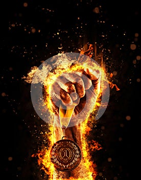 Man`s hand in a fire is holding up gold medal. Winner in a competition.