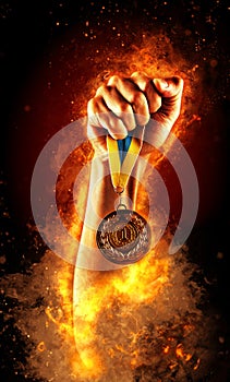 Man`s hand in a fire is holding up gold medal. Winner in a competition.