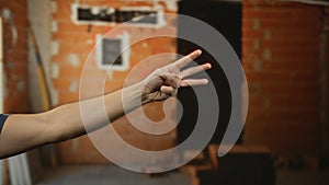 Man\'s hand gesturing three fingers in an indoor construction site, implying a counting or numbering context against a brick photo