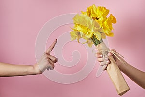 Man`s hand gives bouquet of yellow narcissus flowers to girl and receives refusal, woman shows Attention sign