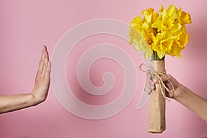 Man`s hand gives bouquet of yellow narcissus flowers to girl and receives refusal, woman shows stop sign