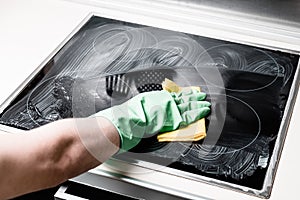 Man`s hand in green glove cleaning cooker at home kitchen