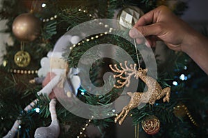 Man`s hand hanging a golden shiny deer on a decorated christmas tree.