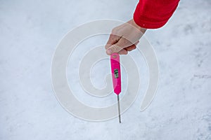 Man`s hand hold a thermometer measuring the temperature of the snow cover