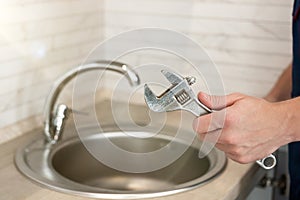 Man`s hand holding adjustable spanner near sink professional plumbing repair service