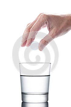 Man`s hand holding an aspirin pill dropping it in a water of glass isolated on white background with clipping path included