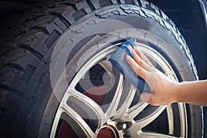 Man's hand holding a blue fabric cleaning car tires and wheels