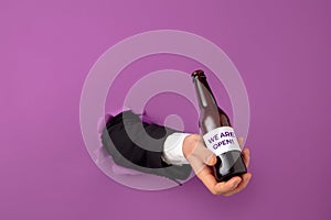 Man& x27;s hand holding bottle of beer breaks through purple background
