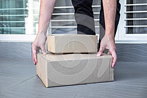 Man`s hand holding boxes at the front door to receive package, shipping delivery concept