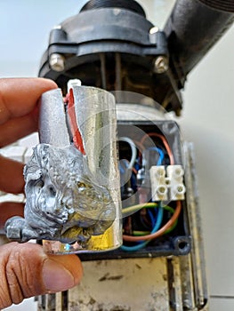 Man's hand holding Broken Capacitor Used On Electric Water Pump.