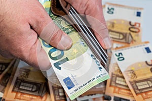 Man`s hand holding a brown wallet with one hundred euro banknote. Many Fifty euro on background