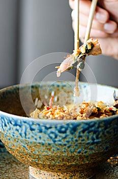 Man`s hand holding chopsticks over a plate of Japanese, thai, chinese meal - rice, mushroom, vegetables. Cafe