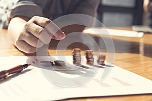 man's hand holding coin with pen and business document on wooden