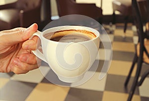 Man`s hand holding a cup of hot coffee with blurry room in background
