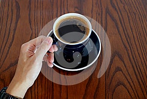 Man`s Hand Holding the Cup of Hot Coffee Served on Wooden Table