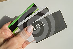 A man& x27;s hand holding a discount card with a 20 percent discount and a copy of the place and several plastic bank cards