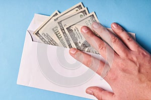 Man`s hand holding dollars in an envelope, top view. Blue background