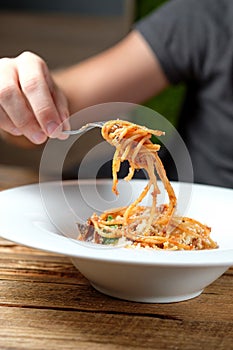 Man`s hand holding a fork with spaghetti over a plate.
