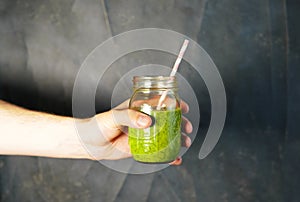 Man`s hand holding a glass jar with berry smoothie on the white wall background.