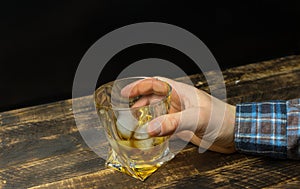 Man`s hand holding Glass of whiskey with ice cubes on rustic wooden table