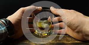 Man`s hand holding Glass of whiskey with ice cubes on rustic wooden table