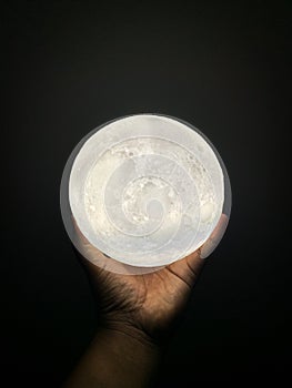 Man\'s hand holding a glowing moon lamp on a dark background