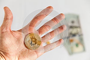 Man`s hand holding golden Bitcoin on background dollars