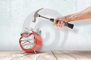 A man`s hand holding a hammer and crashing a retro alarm clock standing on the wooden floor.