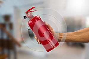 Man`s hand holding handy fire extinguisher on blurred house background