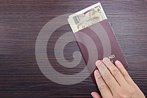 Man`s hand holding international passport and Japanese money on brown dark wooden table