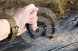 Man`s hand holding knife, compass on old log in the forest.Survival in forest, going on vacation to forest.