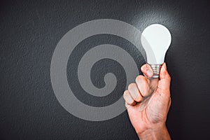 Man`s hand holding LED light bulb over black color wall background, copy space, concept of ideas