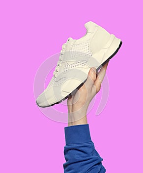 Man's hand holding a modern white sneaker. Sport and active lifestyle. Footwear sales advertising