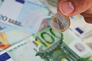 Man's hand holding one euro coin on euro banknotes