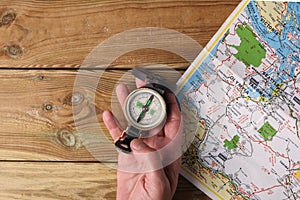 Man`s hand holding an orientation compass on a wooden table with a map and copy space for your text