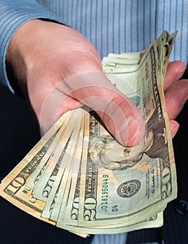 Man`s hand holding out US dollars in ten and twenty dollar bills, close up.