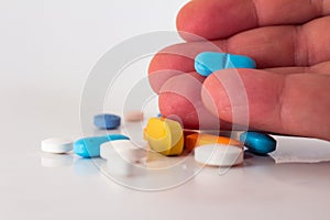 Man`s hand holding a pill. Numerous colorful drugs